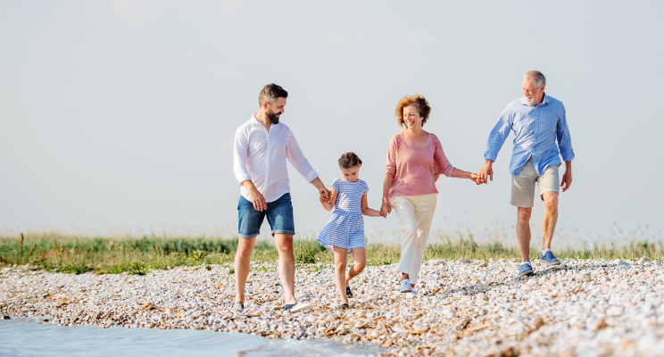 A multigenerational family, ranging from young children to grandparents, walking hand in hand along a pebble-strewn waterside, capturing their shared bond, the texture of the pebbles underfoot, and the serene ambiance of the water's edge.