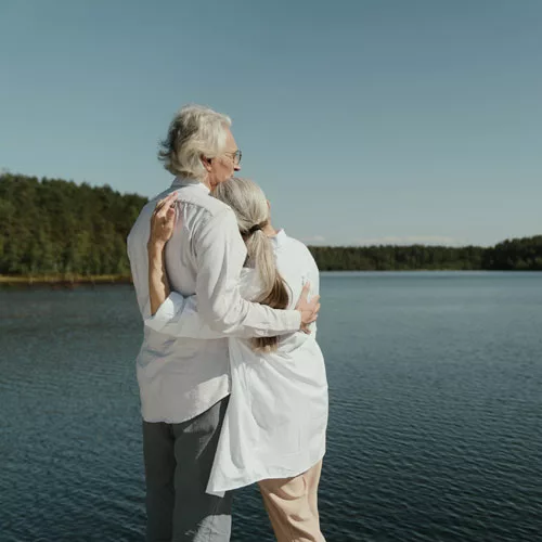 A man and woman, holding each other closely in an embrace, gazing out at a breathtaking mountain lake vista, capturing a moment of shared wonder, connection, and the expansive beauty of nature.